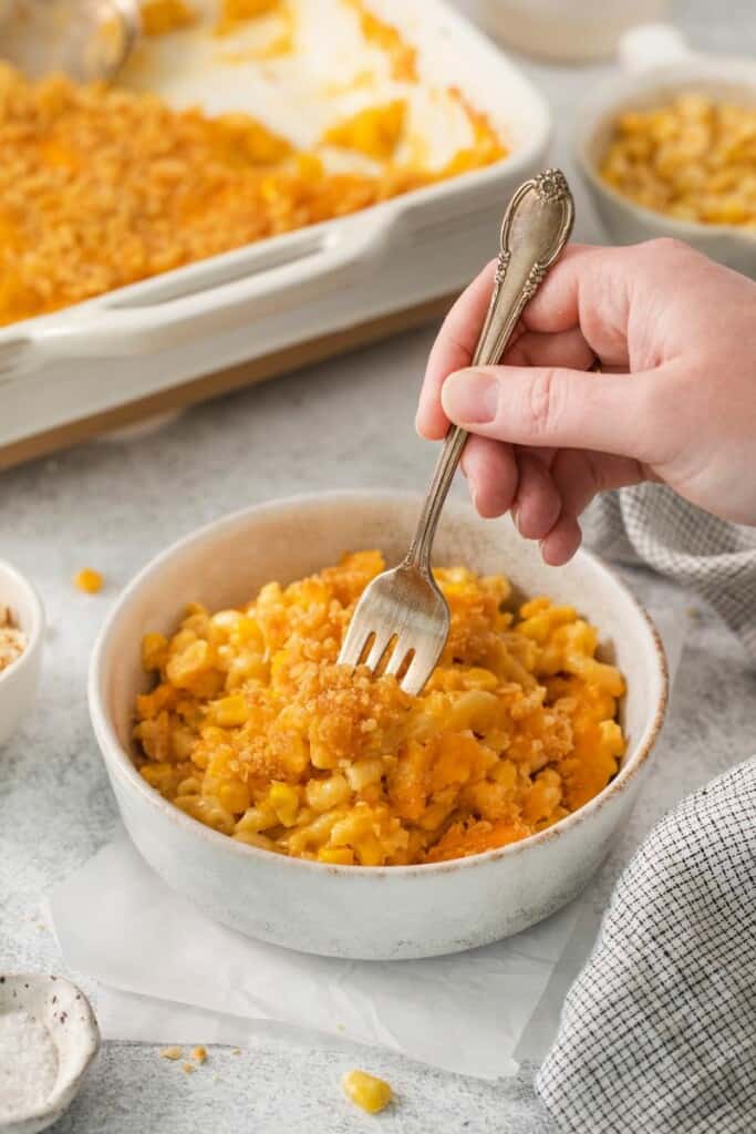 A fork lifting a small bite of corn macaroni casserole from a bowl.