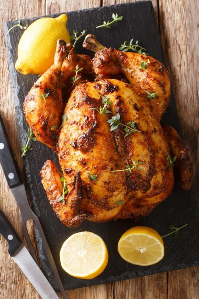 Reheated rotisserie chicken on a black cutting board with lemons and knives