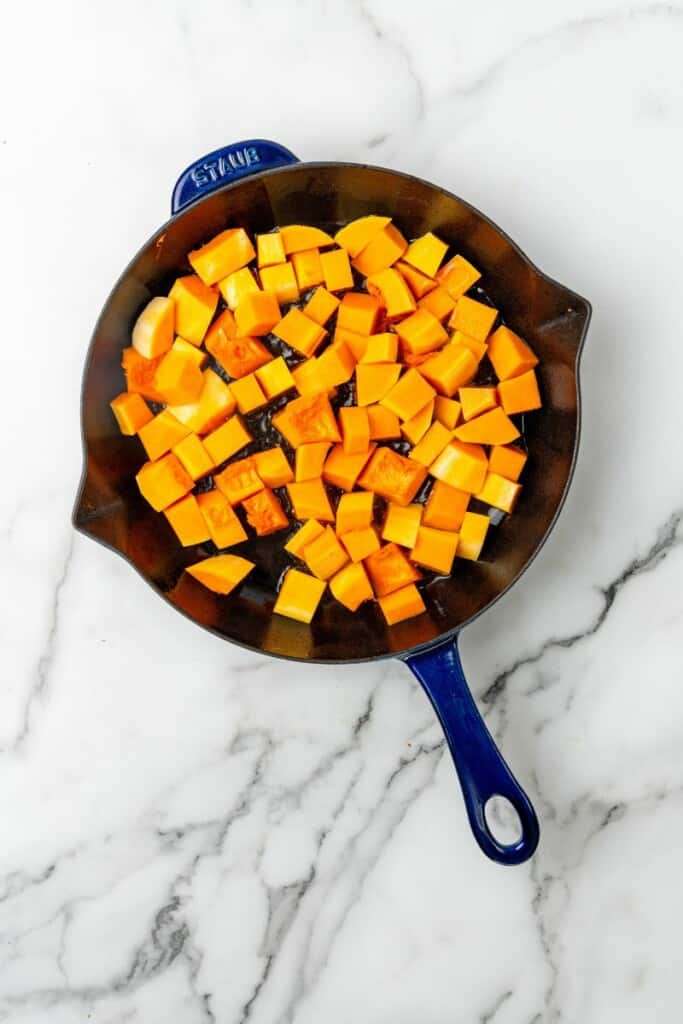 Diced butternut squash pieces in a skillet with oil.
