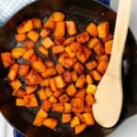 Diced butternut squash that has been sauteed in a skillet with a wooden spoon.
