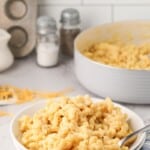 A white bowl of macaroni and cheese with a spoon in it.