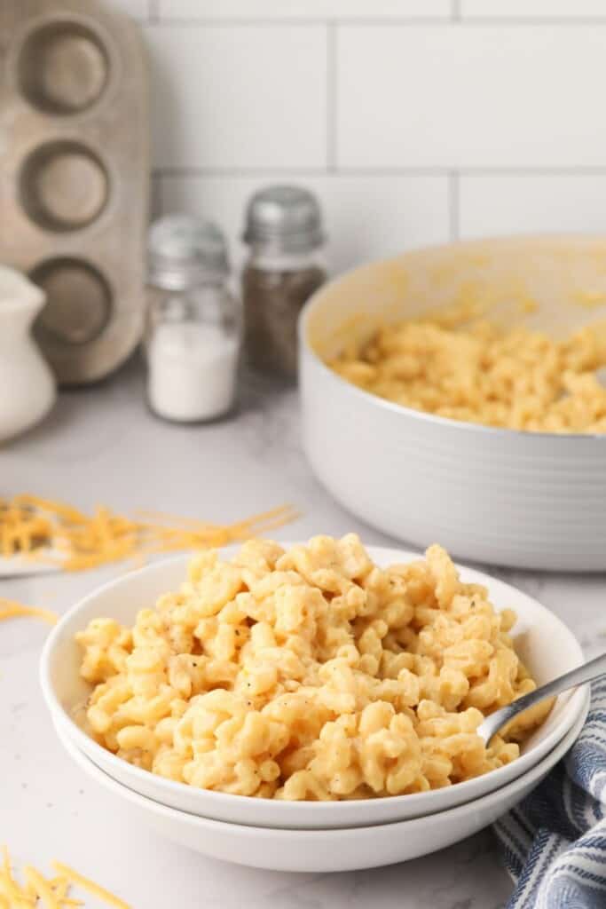 A white bowl of macaroni and cheese with a spoon in it.