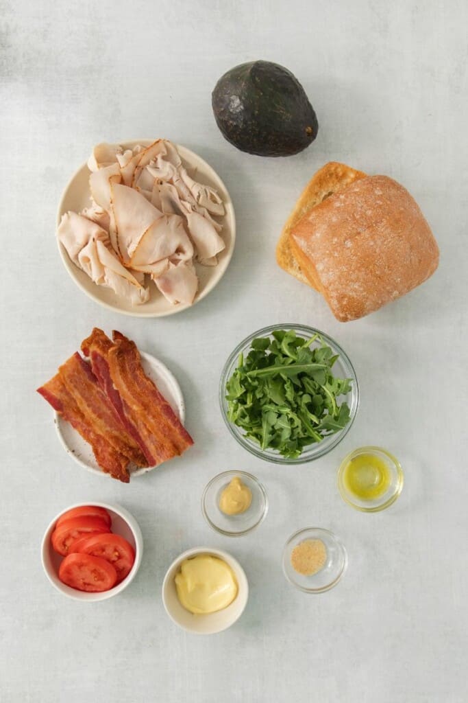 Ingredients needed to prepare a turkey bacon avocado sandwich.