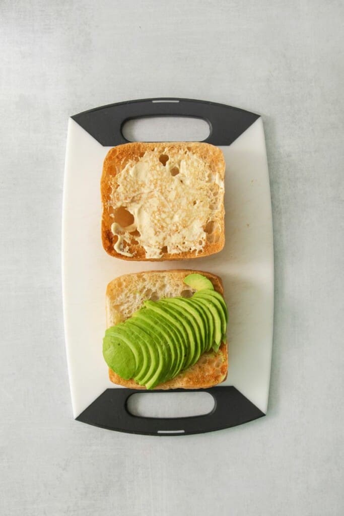2 slices of toasted sourdough with slices of avocado on a cutting board.