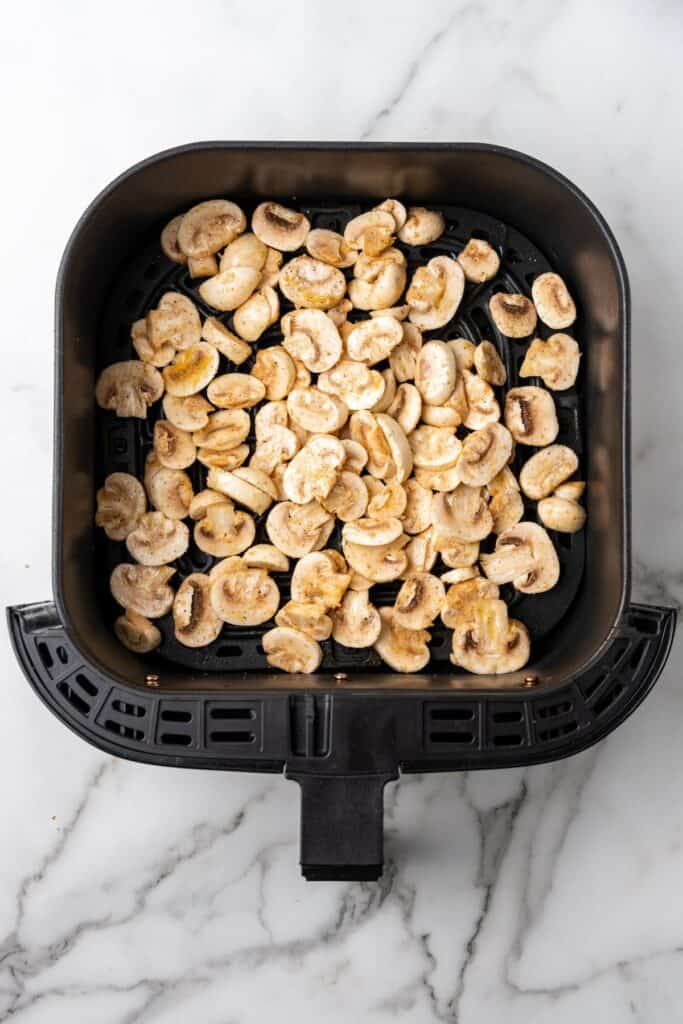 Raw mushrooms in an air fryer basket.