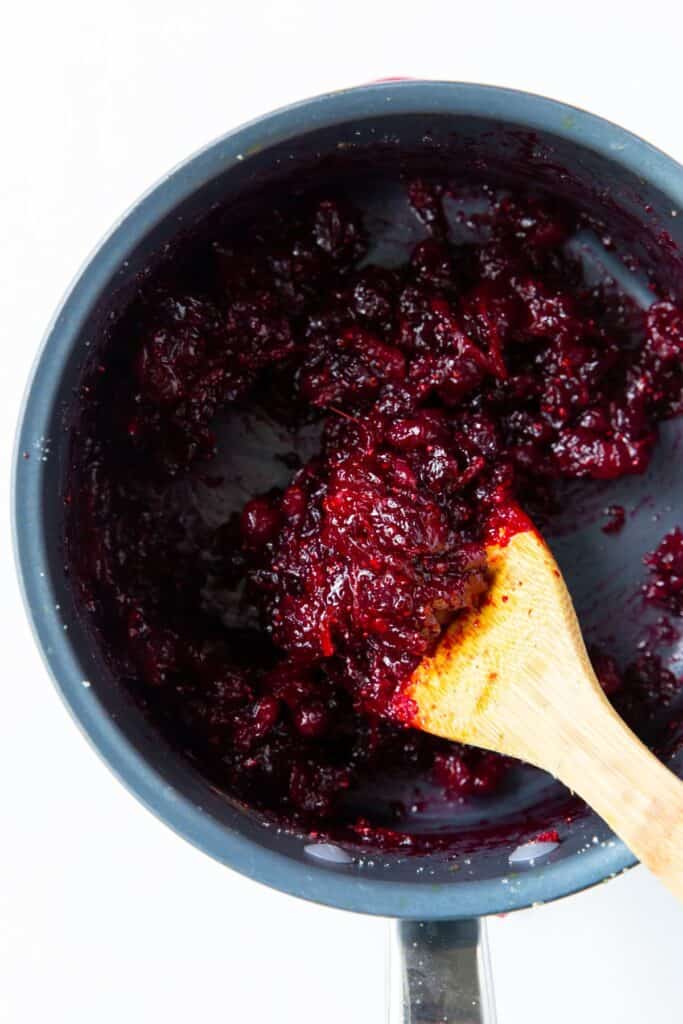 Close up of the cranberry sauce with orange juice in a pot with a wooden spoon stirring it.