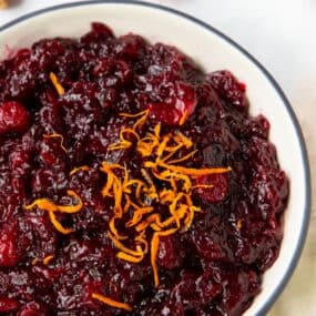 Close up of orange cranberry sauce in a bowl with more orange zest on top.