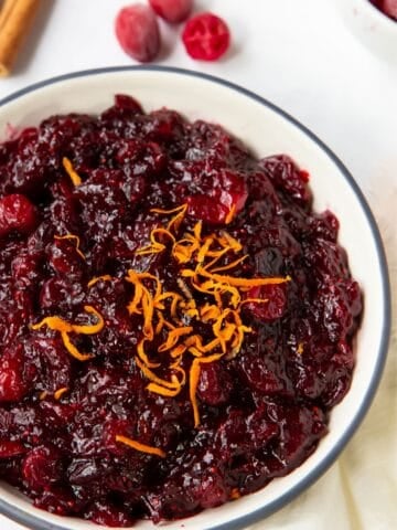 Close up of orange cranberry sauce in a bowl with more orange zest on top.