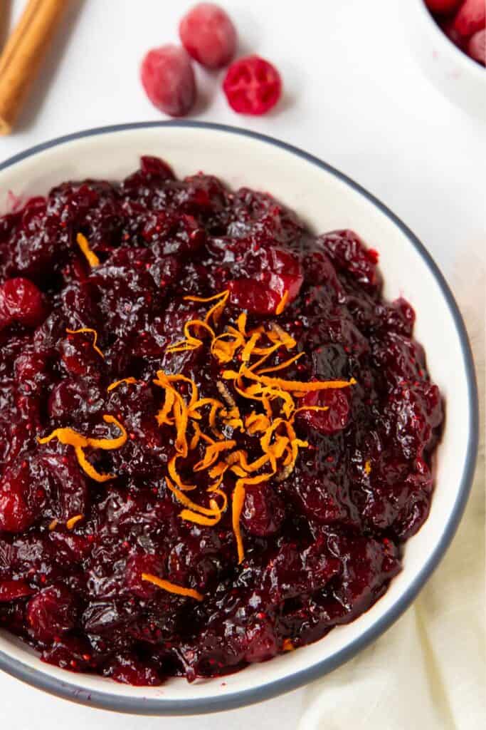 Close up of orange cranberry sauce in a bowl with more orange zest on top.