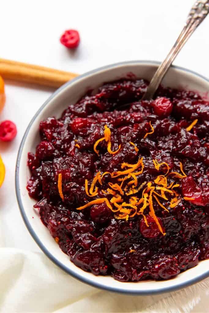 Cranberry orange sauce with extra orange zest on top in a bowl with a spoon in it.