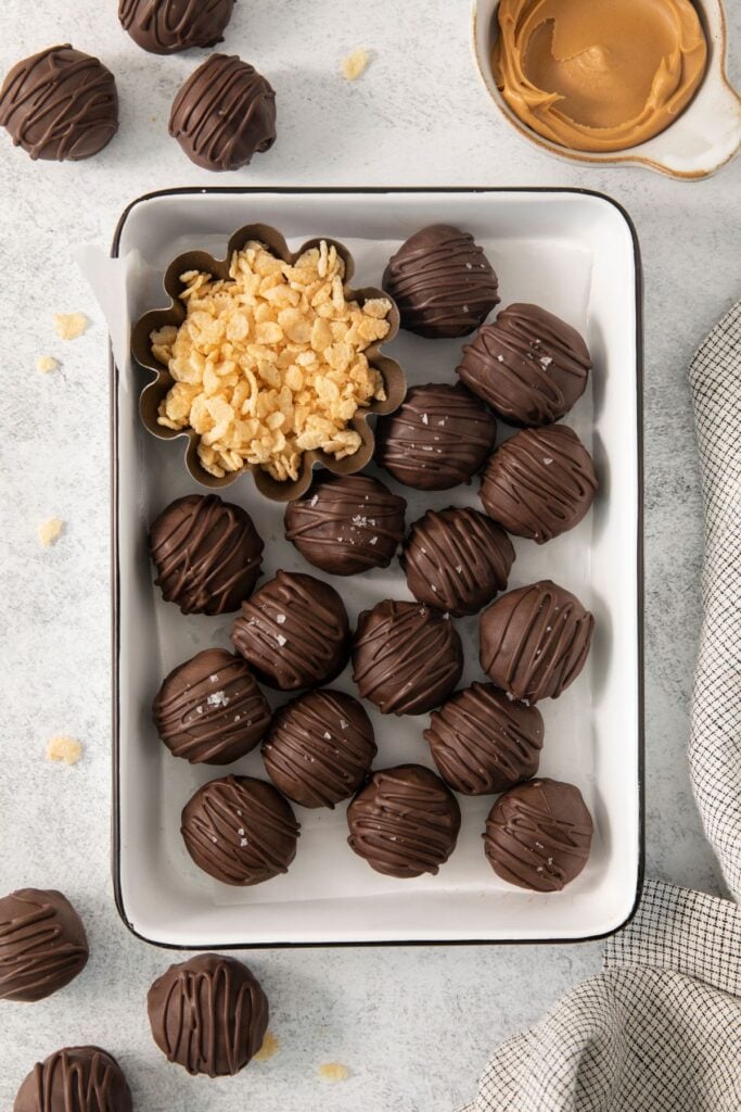Peanut butter balls with rice krispies in a container with a little bowl of rice krispies next to it.