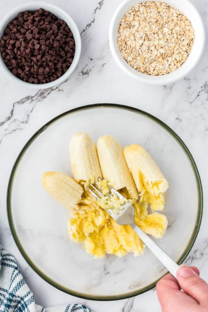 Mashing bananas for oatmeal cookies in a mixing bowl.