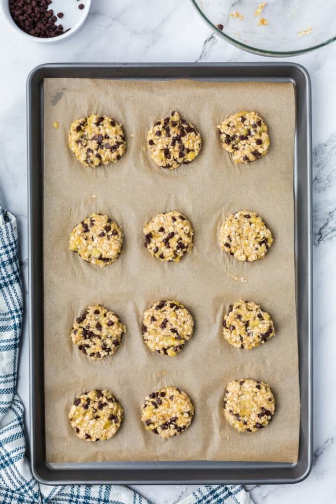 12 oatmeal cookie dough balls on a parchment lined baking sheet.