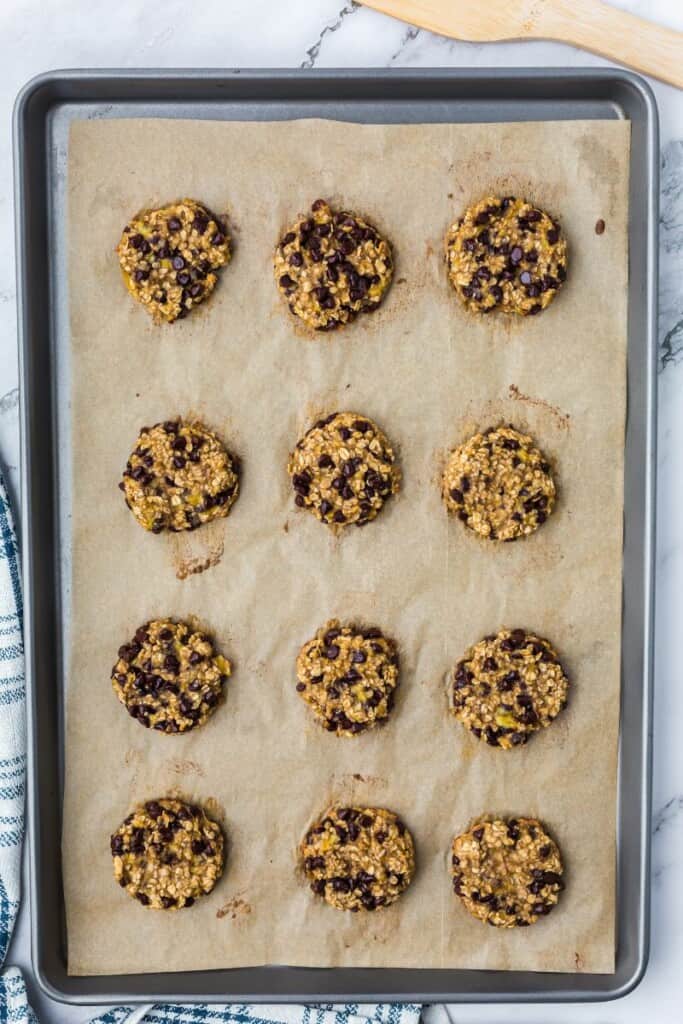 12 baked oatmeal cookies on a parchment lined baking sheet.