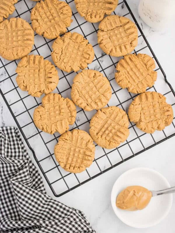 Baked peanut butter cookies on a cooling rack with a spoon holding a bite of peanut butter.