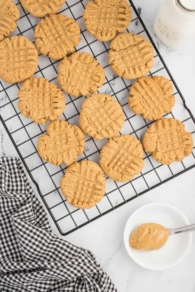 Baked peanut butter cookies on a cooling rack with a spoon holding a bite of peanut butter.