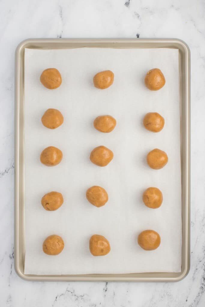 Scoops of peanut butter cookie dough on a parchment lined baking sheet.