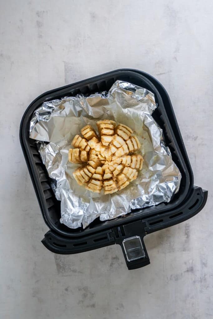 Coated onion on aluminum foil in a black air fryer basket.