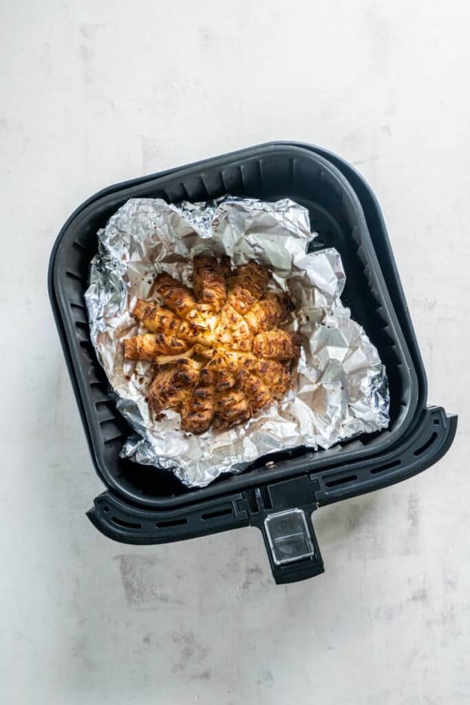 Blooming onion after cooking in an air fryer resting on aluminum foil.