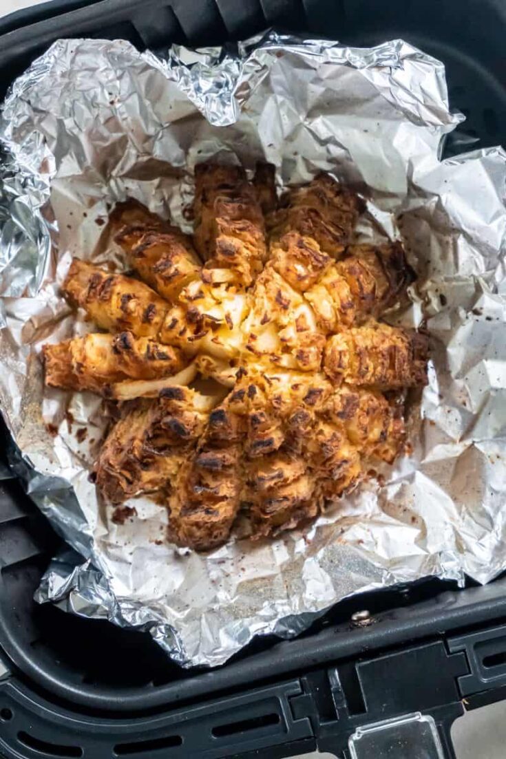 Closeup view of a prepared blooming onion on aluminum foil in a black air fryer basket.