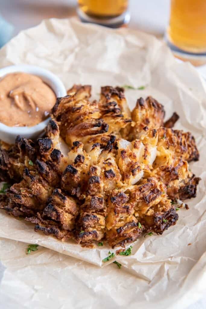 Prepared blooming onion with dipping sauce on parchment paper.