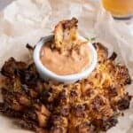 A prepared blooming onion with dipping sauce on parchment paper.