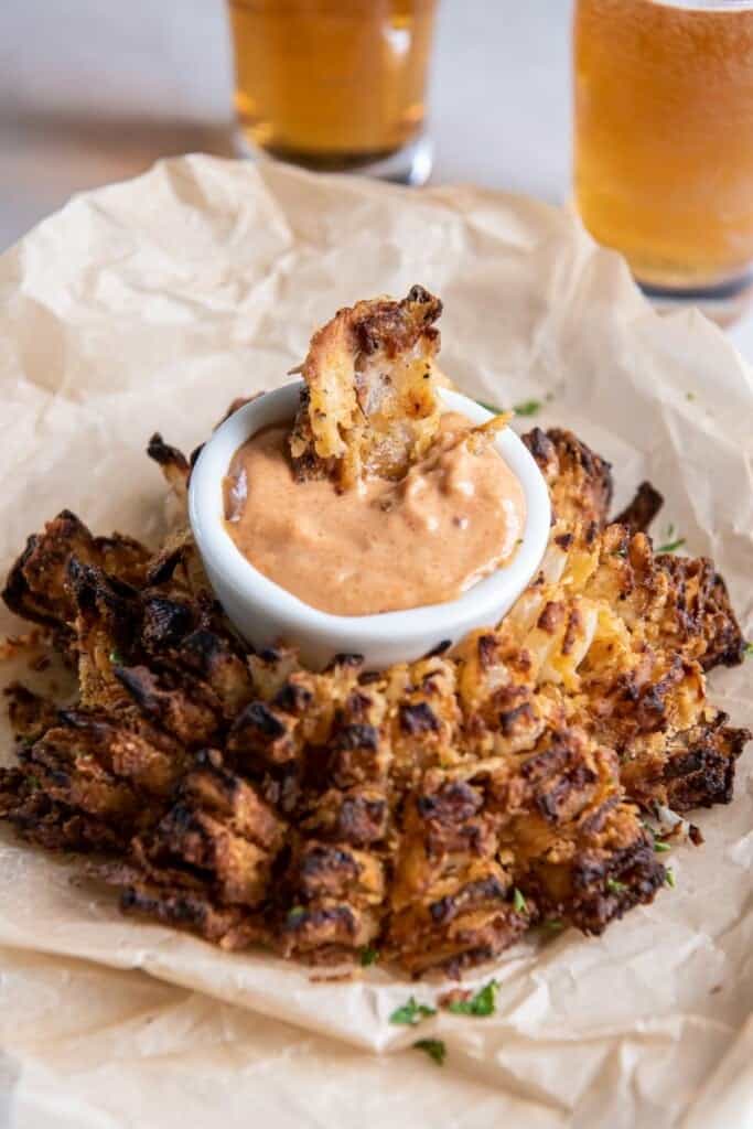 A prepared blooming onion with dipping sauce on parchment paper.