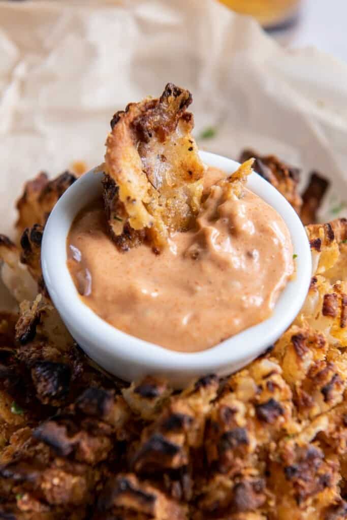 Closeup view of a piece of blooming onion dipping into sauce.