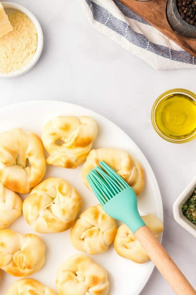 Brushing olive oil with seasoning mixture over prepared garlic knots.