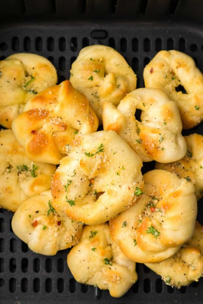 Close up view of prepared garlic knots with seasoning resting in a black air fryer basket.