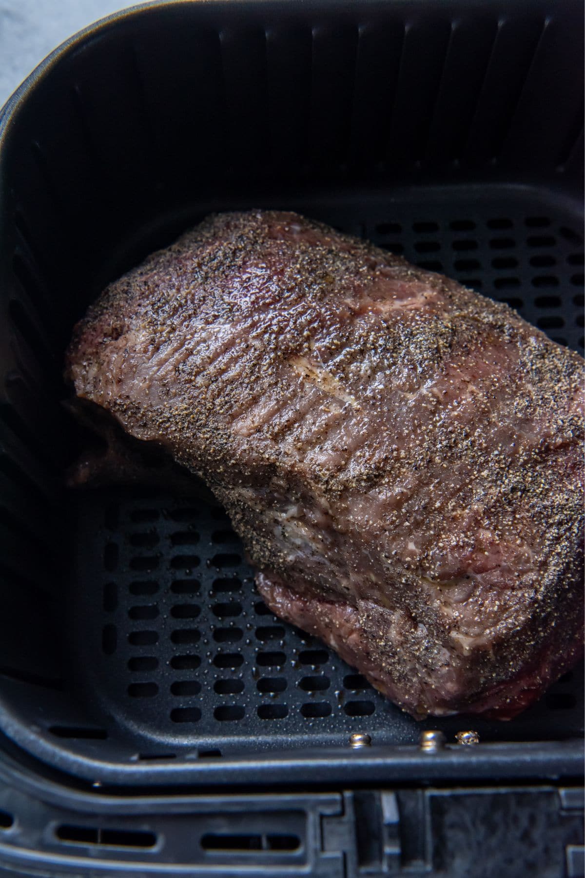 Raw seasoned roast beef in an air fryer basket.