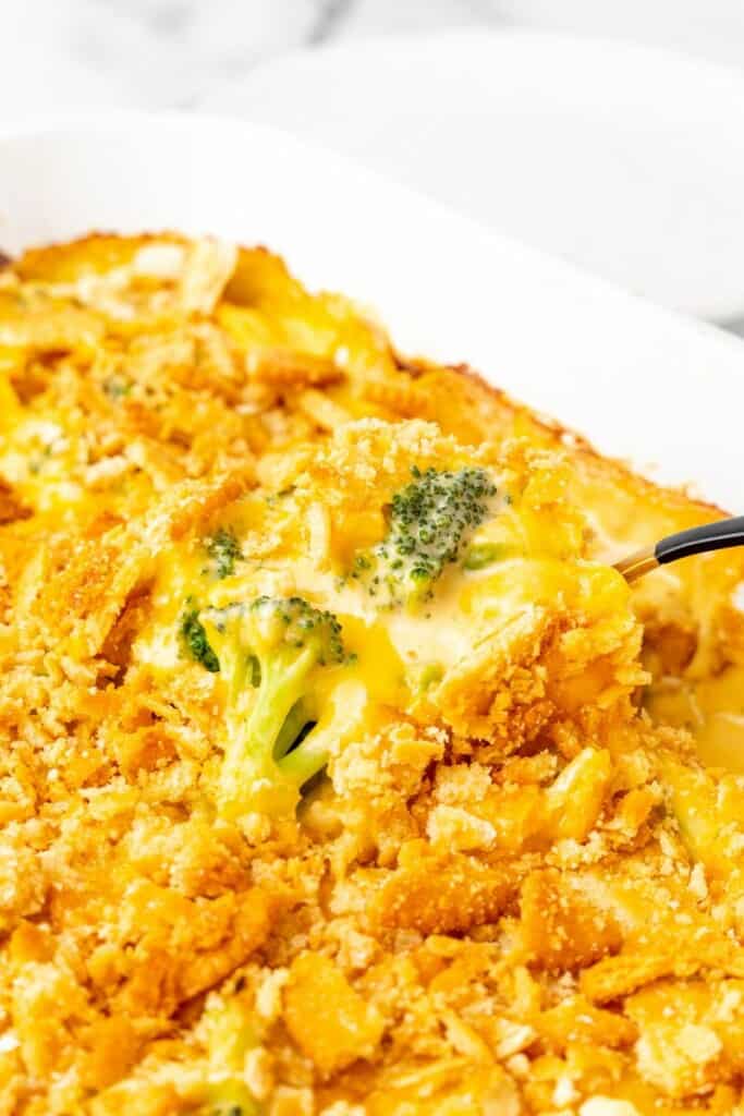 A spoon lifting a bite of broccoli cheese casserole from the dish.