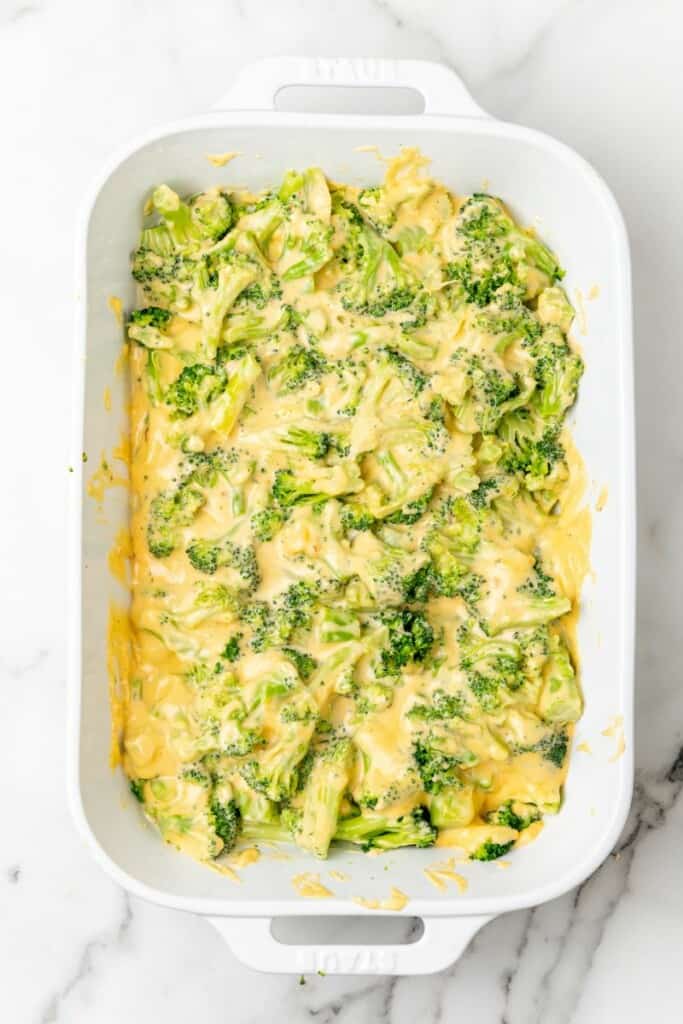 Adding cheese sauce to broccoli in a casserole dish.