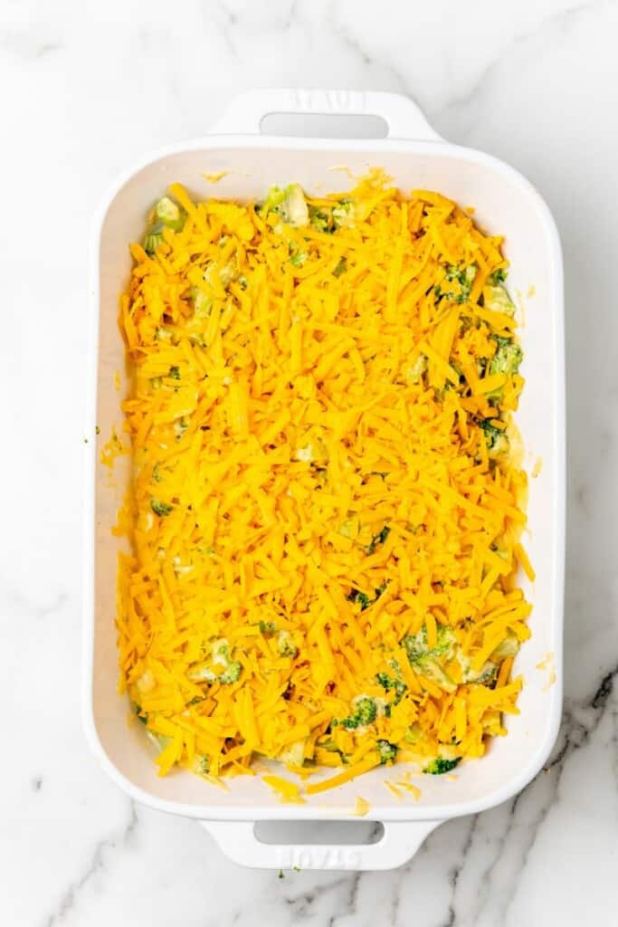 Shredded cheese sprinkled over broccoli and cheese mixture in a casserole dish.