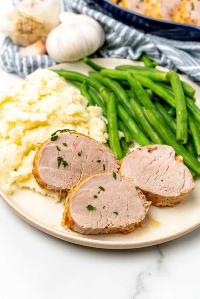 Three slices of pork tenderloin plated with mashed potatoes and green beans.