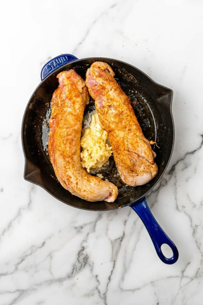 Seasoned pork tenderloin cooking in a cast iron skillet.