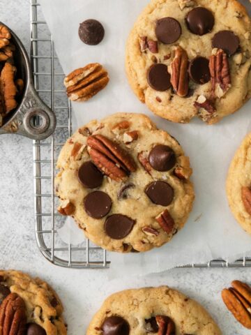 A few chocolate chip cookies with pecans on a cooling rack.