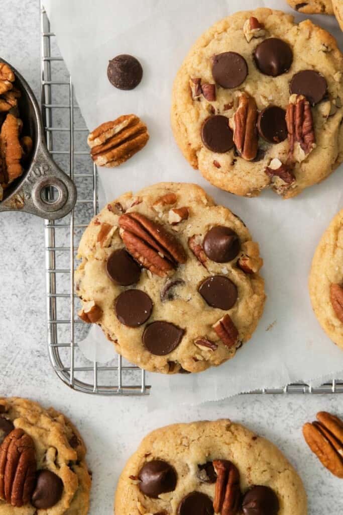 A few chocolate chip cookies with pecans on a cooling rack.