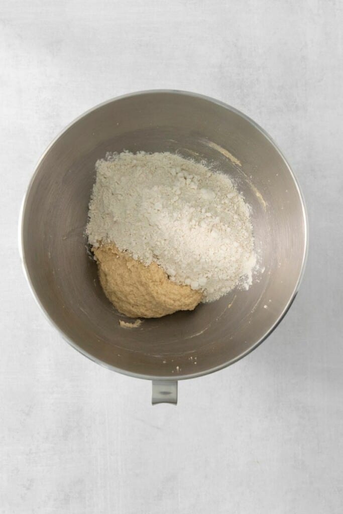 Adding flour to cookie base mixture in a mixing bowl.