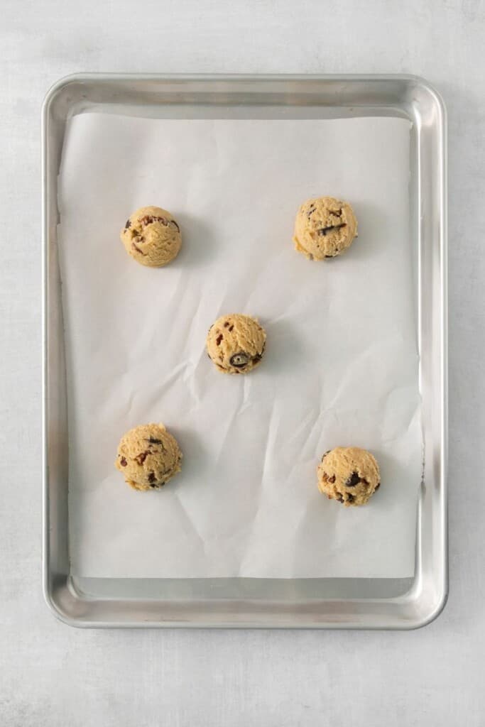 Five cookie dough balls on a baking sheet lined with parchment paper. 