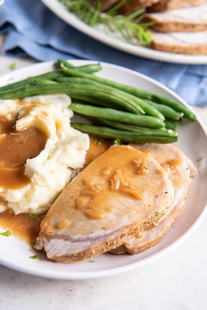 Closeup view of pork loin slices with gravy on a plate with mashed potatoes and green beans.