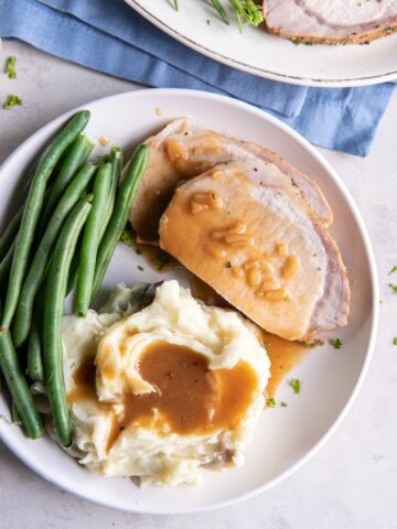 Pork Loin with gravy on a plate with mashed potatoes and green beans.