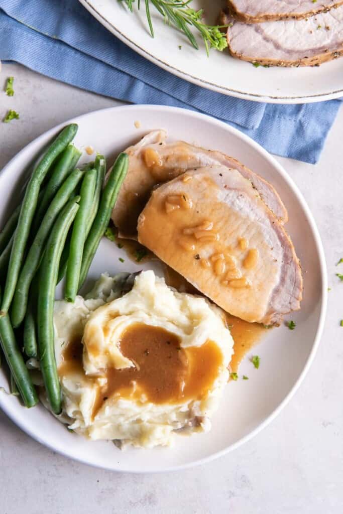 Pork Loin with gravy on a plate with mashed potatoes and green beans.