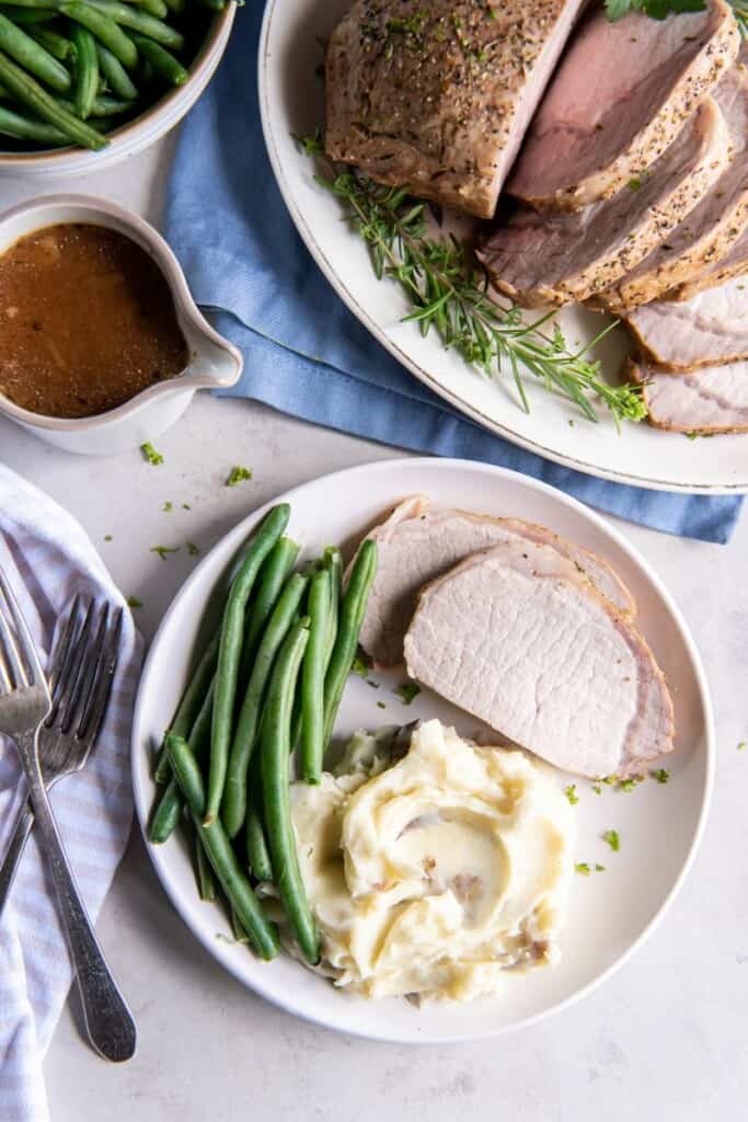 Slices of pork loin with mashed potatoes and green beans on a plate.