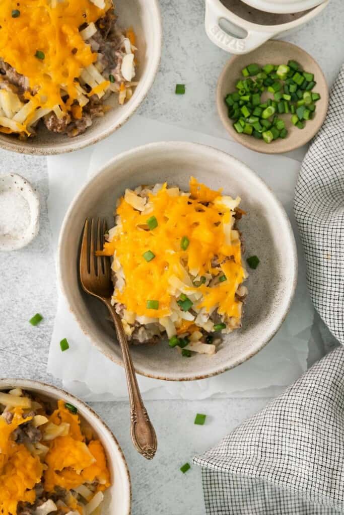 A serving Cheesy Hamburger Hash Brown Casserole in a bowl with a fork.