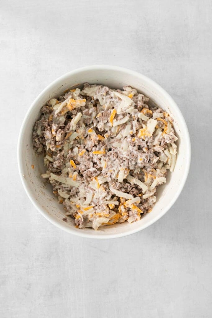 Combining ingredients for hamburger hash brown casserole in a mixing bowl.