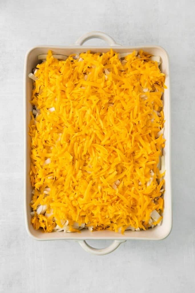 Adding shredded cheese to the top of hamburger hash brown casserole in a baking dish.