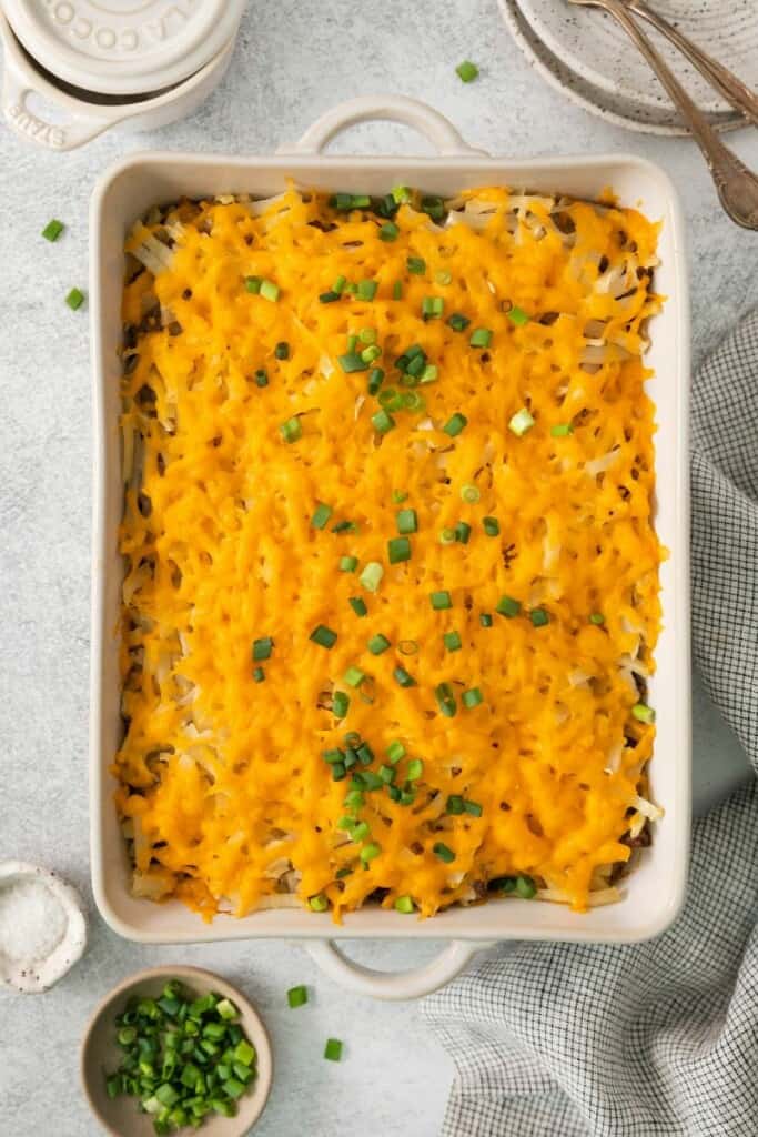 Baked hamburger hash brown casserole garnished with green onions in a baking dish.