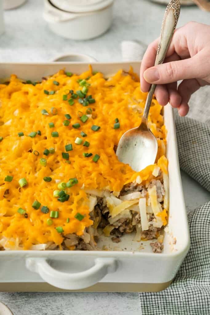 A closeup view of a baking dish containing hamburger hash brown casserole with one serving removed.