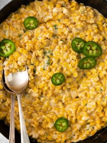 Jalapeno cream corn topped with additional jalapeno slices in a cast iron skillet with a spoon.
